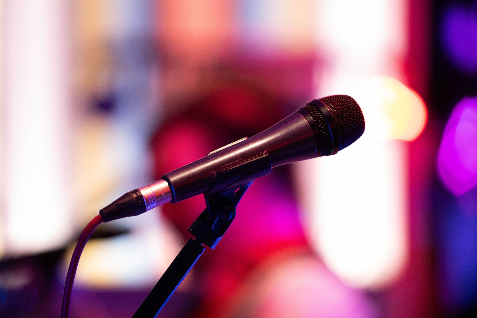 Close-up shot of a microphone on stage with colorful background bokeh, capturing live performance ambiance.